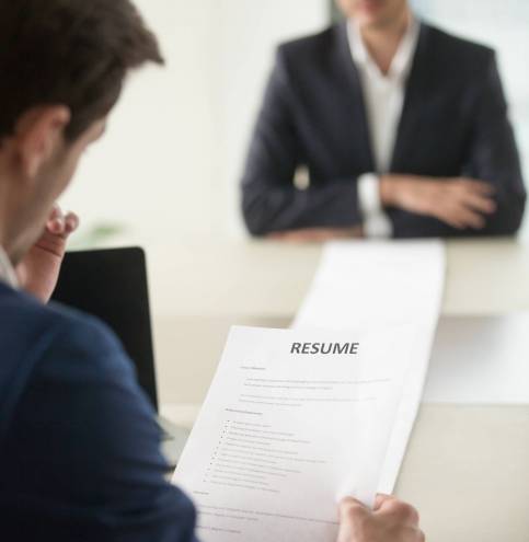 Interviewer reading applicants long resume Back view of employer reading resume focus on document, job applicant waiting for hiring decision at desk on background. Hiring manager studying long list of candidates achievements and experiences