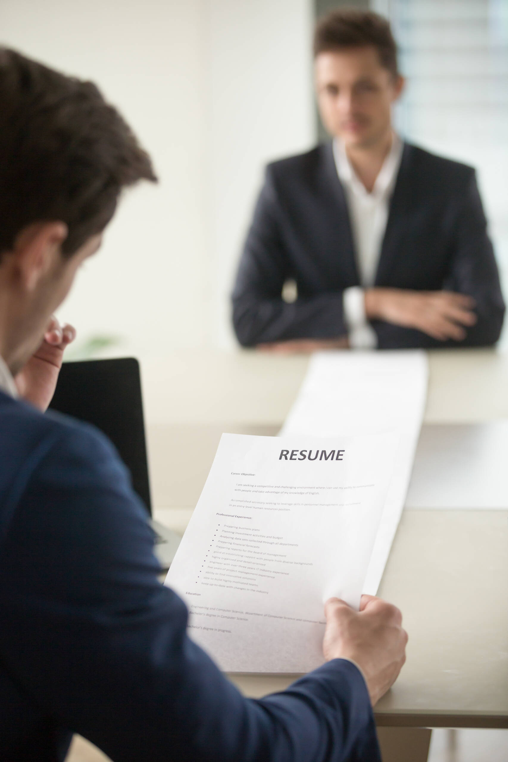 Interviewer reading applicants long resume Back view of employer reading resume focus on document, job applicant waiting for hiring decision at desk on background. Hiring manager studying long list of candidates achievements and experiences